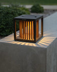 Modern outdoor solar lantern on a concrete surface with greenery in the background