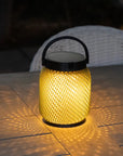 Yellow woven solar lantern with black handle on a wooden surface by Les Jardins available at Spacio retail stores in Mumbai & Kolkata.  
