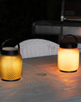 Two illuminated outdoor solar lanterns on a patio table with a blurred background
