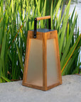 Wooden solar lantern with a handle on a stone surface with greenery in the background