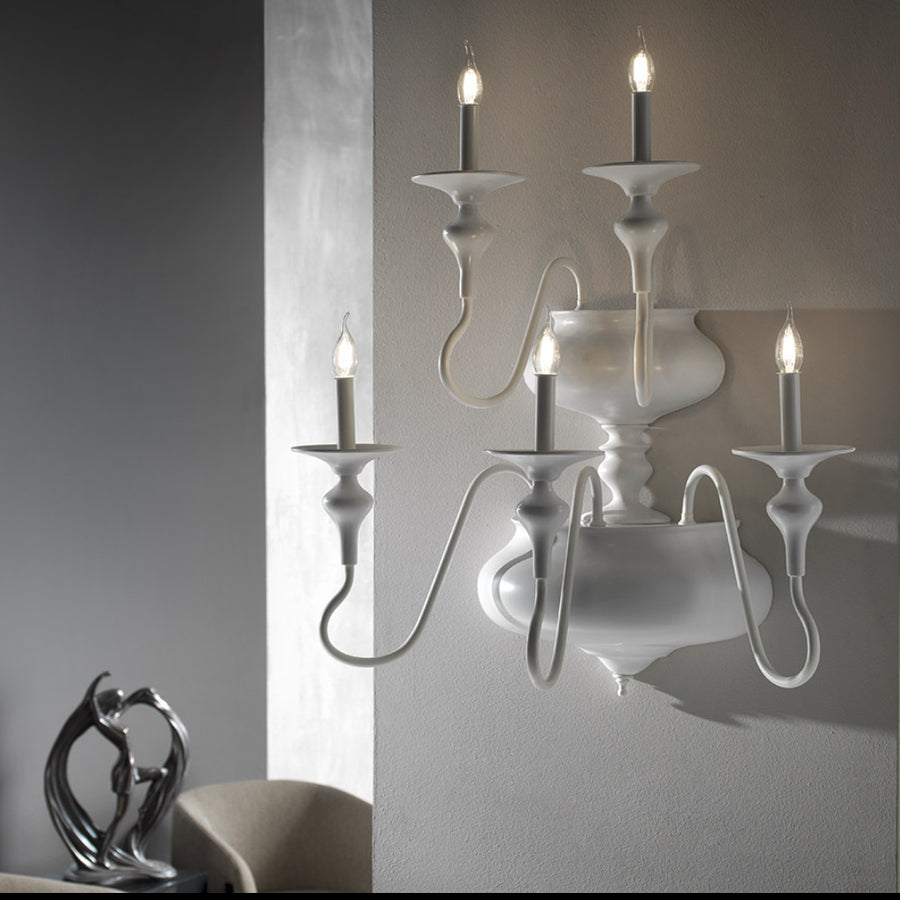 White wall-mounted candle holder with four lit candles against a neutral background
