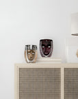 Two decorative crystal masks on a shelf with a lamp in the background