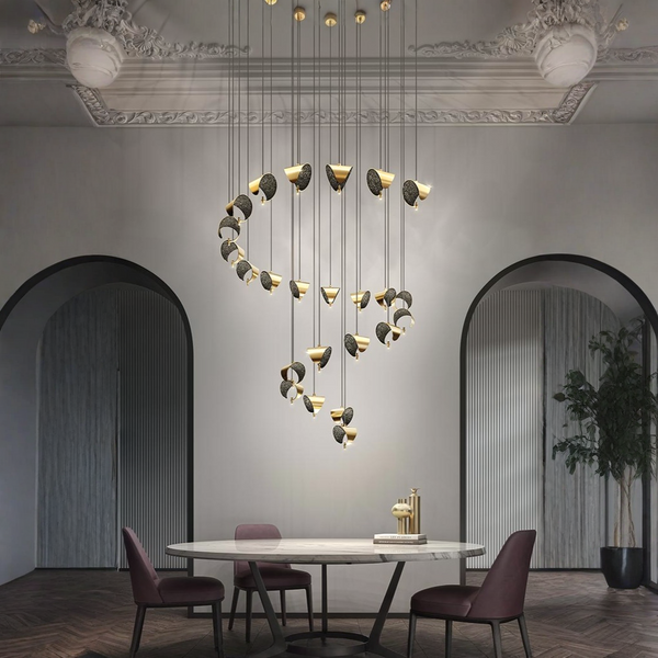A modern multi-light pendant chandelier with gold and black sculptural leaf-like shades hangs over a dining table in a stylishly decorated dining room with arched doorways and a potted plant.