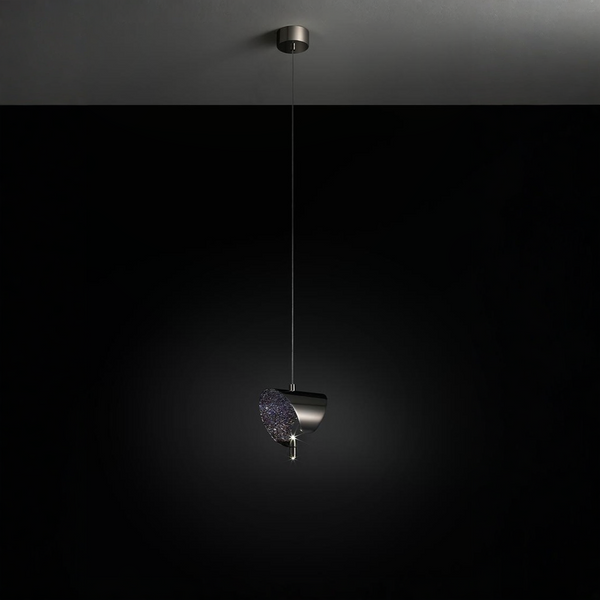 A modern pendant light fixture with a dark metallic cylindrical shade and a textured, glittery purple glass shade, suspended by a thin cord from a matching ceiling canopy against a dark background.