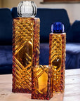 Set of three decorative glass vases & votive holder on a wooden surface with a blurred blue sofa in the background