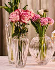 Clear crystal vases with pink flowers on a tablecloth by Mario Cioni, available at Spacio retail stores in India. 