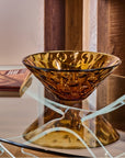 Amber crystal bowl on a reflective surface with a blurred background