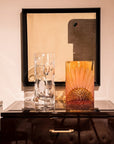 Two crystal vases on a reflective surface with a framed abstract artwork in the background.