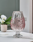 Decorative crystal vase with red speckles on a marble surface with a blurred background