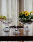 Two crystal bowls with decorative items on a table against a curtain background