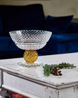Decorative crystal bowl with gold base on a white wooden table in a living room setting.