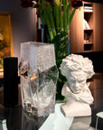 Crystal vase and white sculpture on a reflective surface with a blurred background