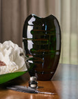 Green crystal vase with white flowers and a feather on a wooden surface