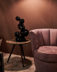 Pink armchair and black abstract crystal sculpture in a room with brown walls.