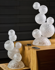 Decorative crystal sculptures in 2 sizes with marble-like texture on a wooden surface against a dark brick wall.