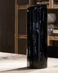 Black cylindrical crystal vase on a marble surface with a blurred background