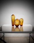 Distant look of Mario Cioni Crystal Amphorae Deep Amber Vases Set on a Large Table available at Spacio India for luxury home decor collection of decorative vases.