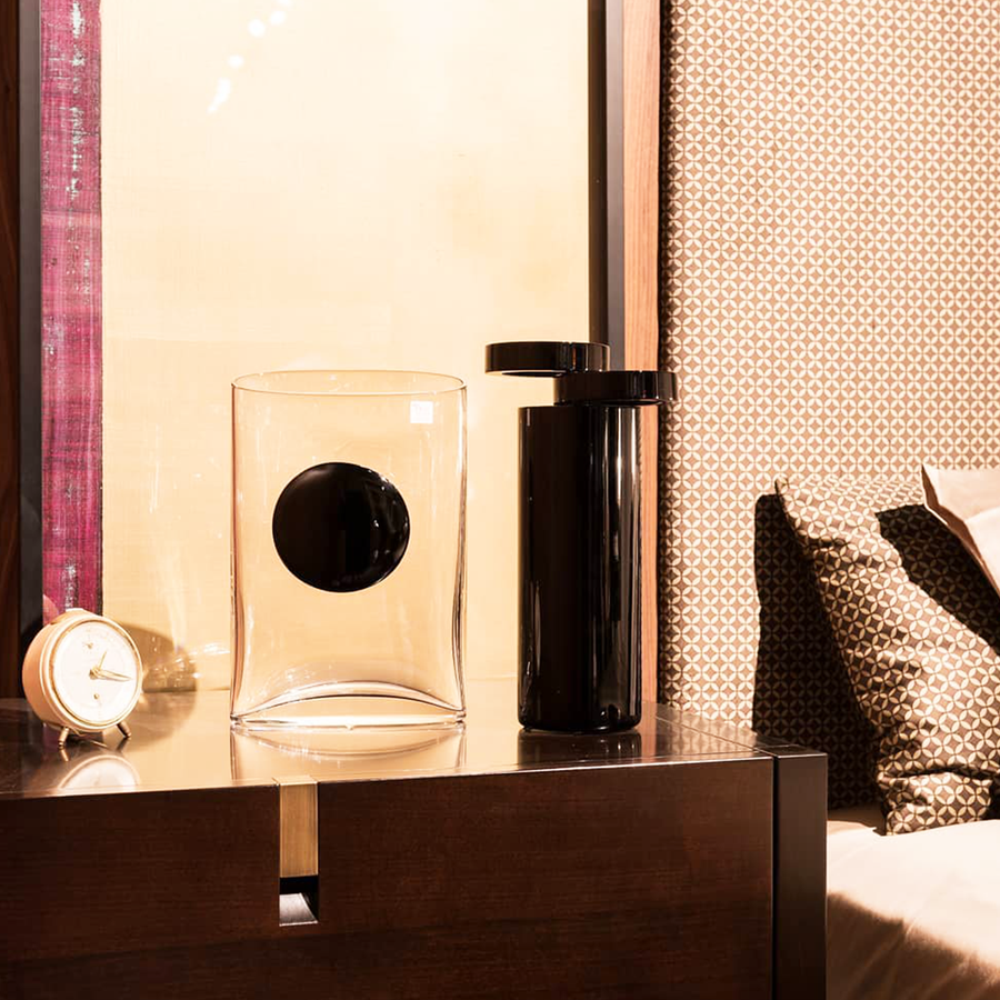 Mario Cioni A.Y.L.I. Cilindric Black Crystal Vase by Tondo Doni on a side table with a vase & table clock in bedroom interior available at spacio india for luxury home decor collection of decorative vases.