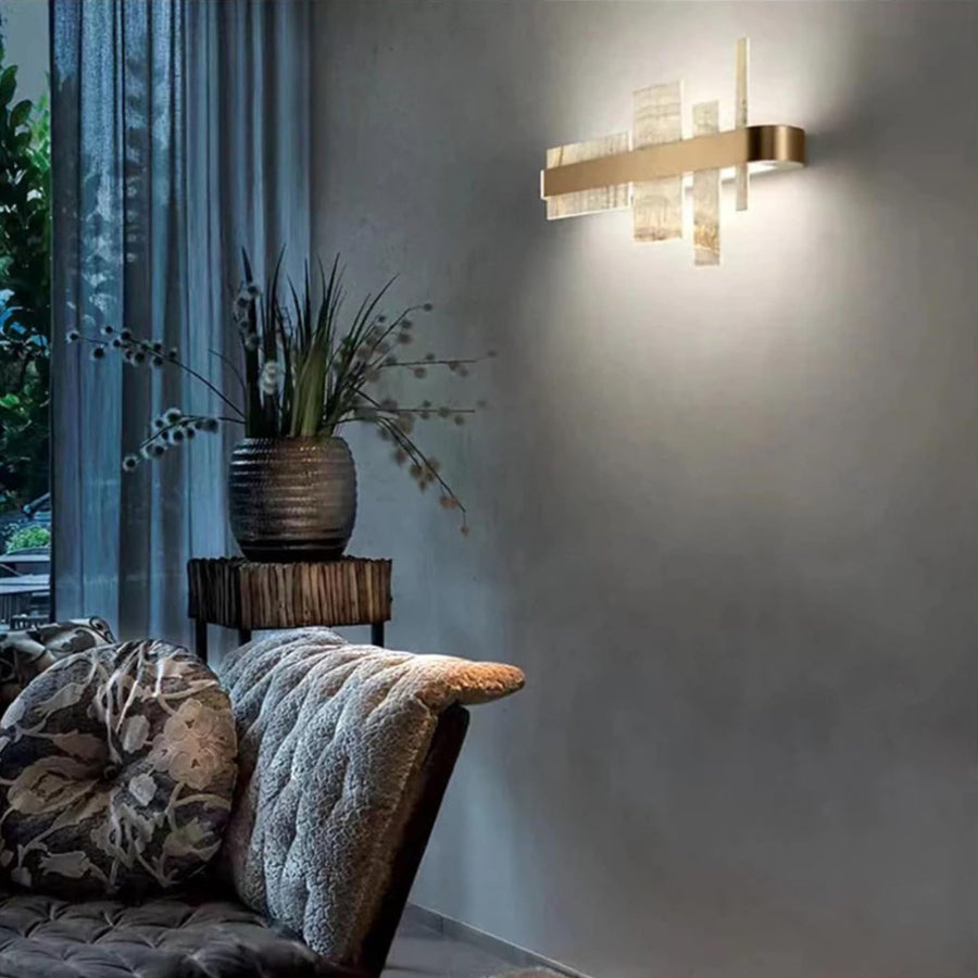 Modern wall sconce lighting fixture  by Masiero available at Spacio retail stores in Mumbai & Kolkata, on a gray wall with a plant and cushioned chair in the foreground.