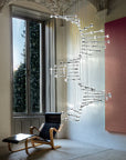 Modern chandelier hanging in a room with a window and chair.