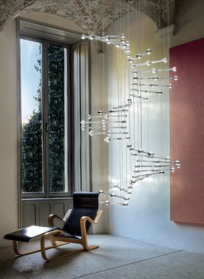 Modern chandelier hanging in a room with a window and chair.