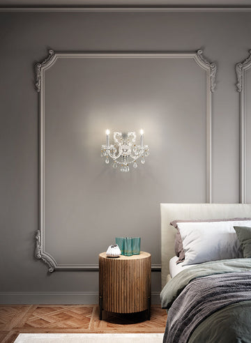 Aqaba crystal chandelier by Masiero from Spacio on a wall behind a neatly made bed with a wooden side table