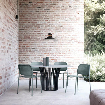 Modern outdoor dining set with a round table and chairs against a brick wall and Masiero's Cordea outdoor pendant light