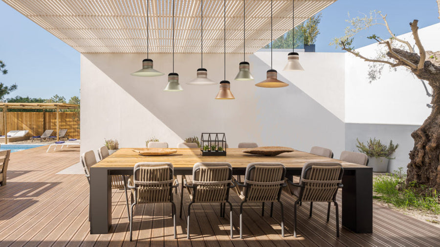 Outdoor dining area with a large table and chairs on a wooden deck and Masiero's Cordea outdoor pendant lights in different colours hanging from wooden slatted ceiling. 