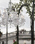 Outdoor chandelier hanging in front of a bridge with trees and street lamps in the background