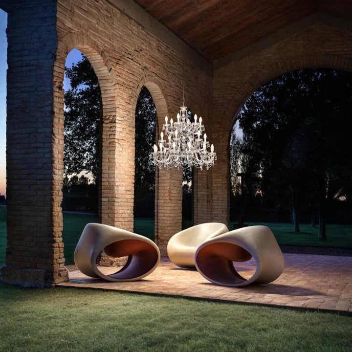 Modern outdoor chairs under an outdoor chandelier from Masiero's Drylight collection in an archway with trees in the background