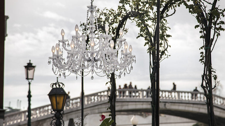 Outdoor chandelier hanging in front of a bridge with trees and street lamps in the background