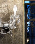 Outdoor Crystal wall sconce on a textured wall with decorative metal gate in the background from Masiero's Drylight collection available at Spacio