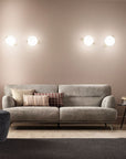 Gray sofa with decorative pillows in a modern living room setting and Posy wall light from Masiero available at Spacio in India. 