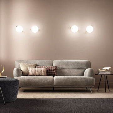 Gray sofa with decorative pillows in a modern living room setting and Posy wall light from Masiero available at Spacio in India. 