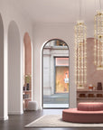 Modern interior design with arched doorways, a pink round ottoman, and hanging crystal lights.