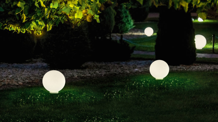Glowing spherical garden lights in a garden setting with trees and grass.