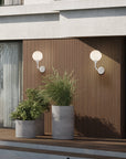 Modern outdoor setting with wall lights and potted plants in front of a building.