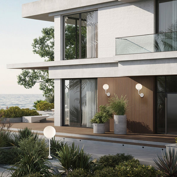 Modern house exterior with large windows, plants, and a view of the ocean and outdoor wall lights by Masiero