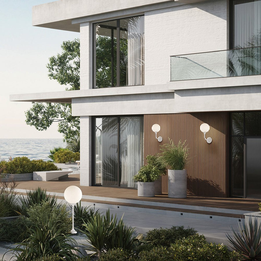 Modern house exterior with large windows, plants, and a view of the ocean and outdoor wall lights by Masiero