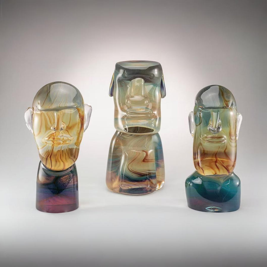 Three colorful Murano glass sculptures of stylized faces on a gray background