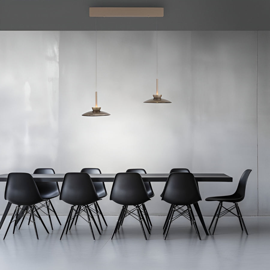 Modern black chairs around a dining table with pendant lights in a minimalistic setting.