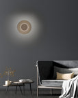 Modern wall light fixture on a dark gray wall with a sofa and side table in the foreground.