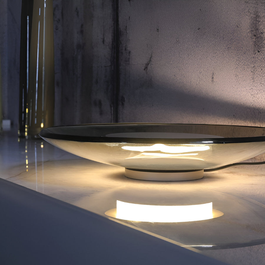 Glass table lamp on a reflective surface with a dark background