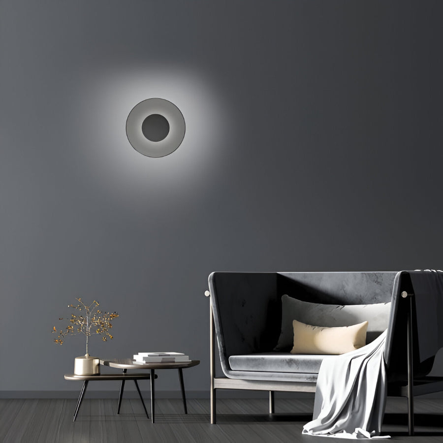Modern wall light fixture on a dark gray wall with a sofa and coffee table in the foreground.
