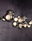 Modern kinetic chandelier with multiple light bulbs against a dark textured wall