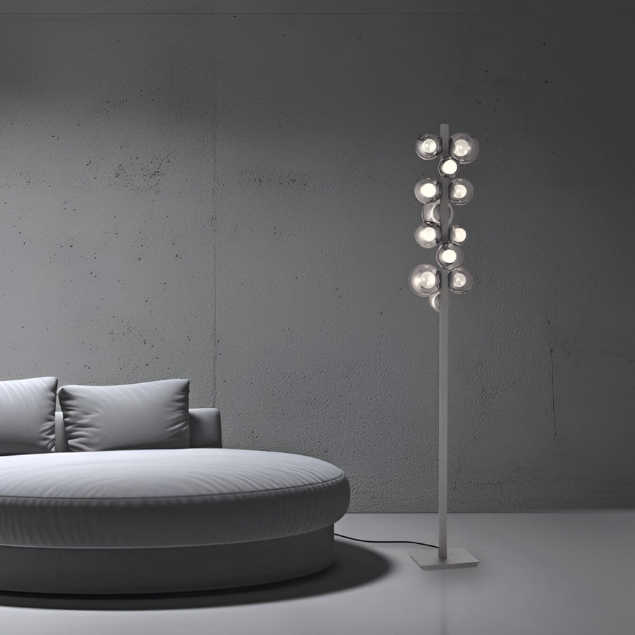 Modern floor lamp with multiple bulbs next to a round gray sofa against a gray wall.