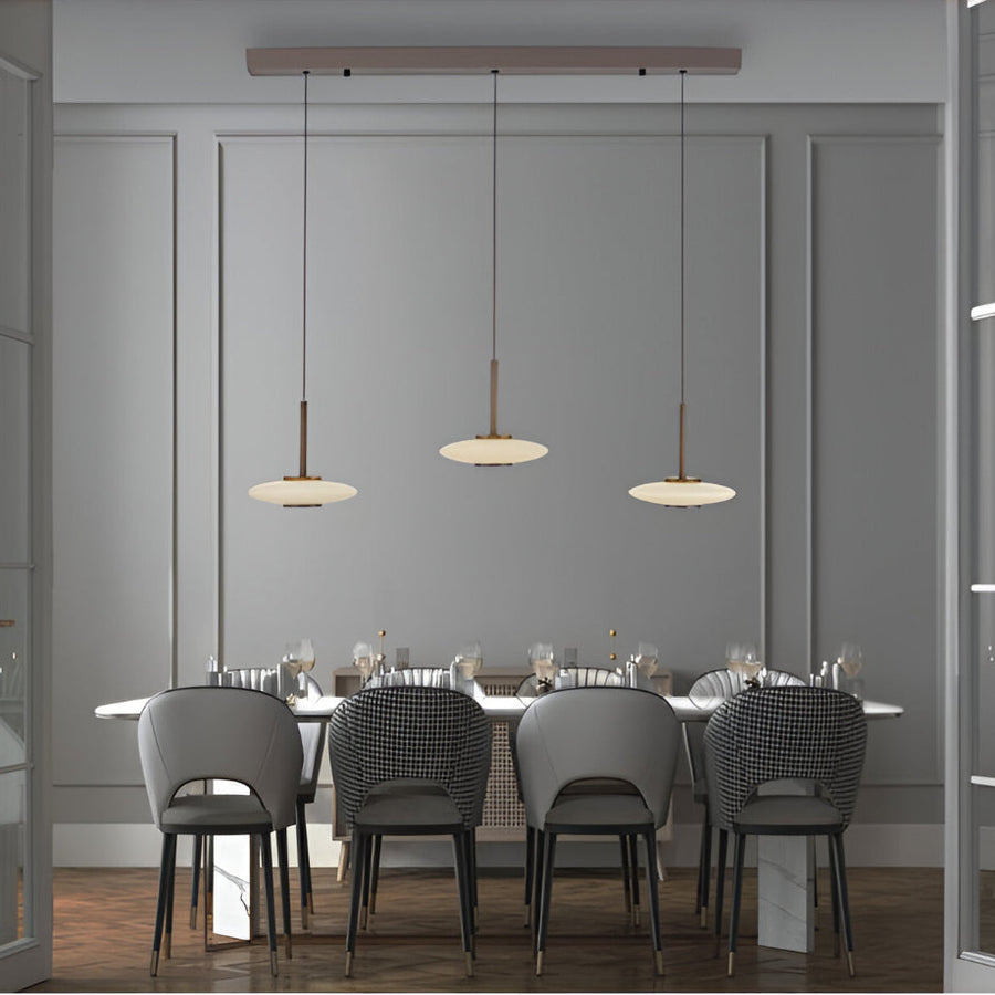 Dining area with gray chairs and a long table under pendant lights in a modern interior.