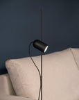 Modern black floor lamp against a dark blue wall with a beige sofa.