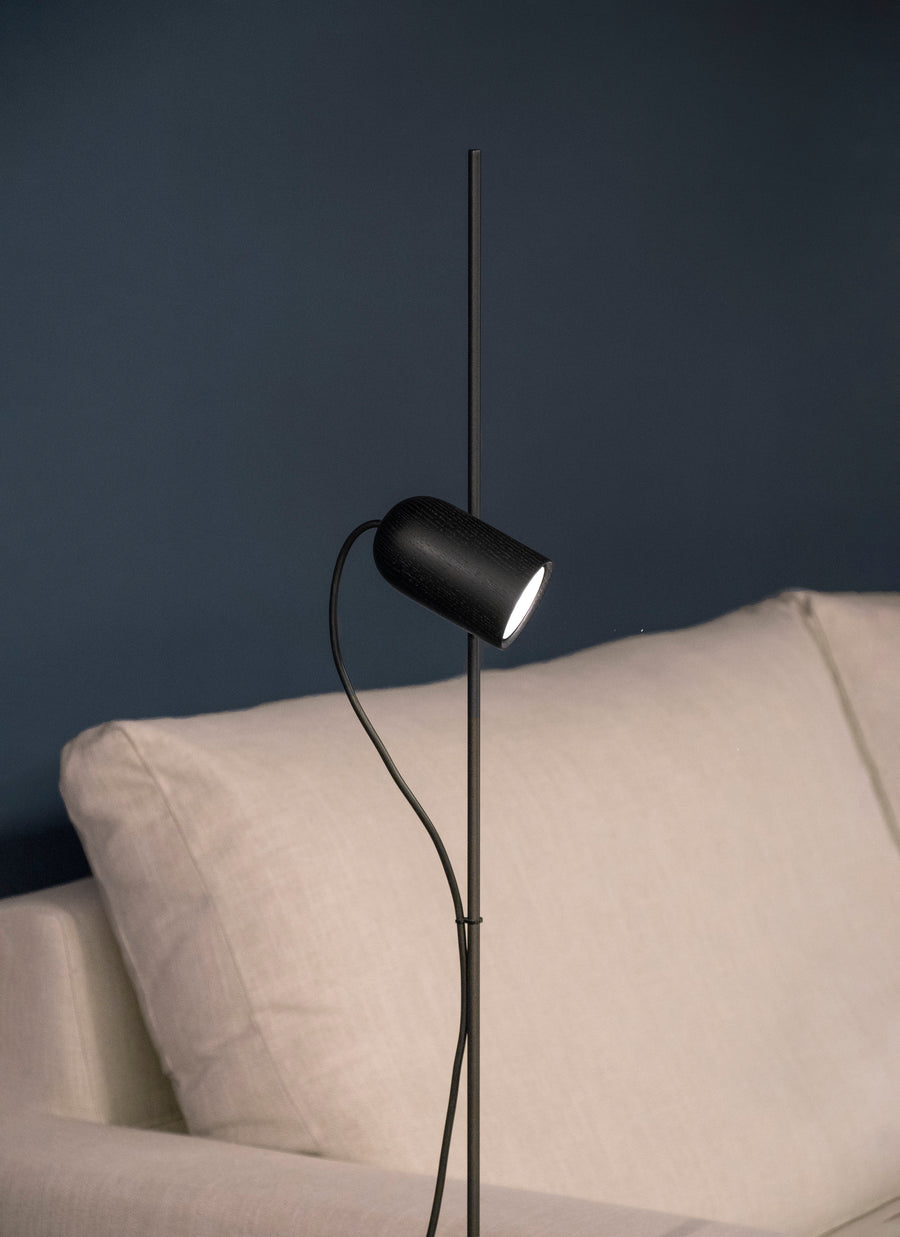 Modern black floor lamp against a dark blue wall with a beige sofa.