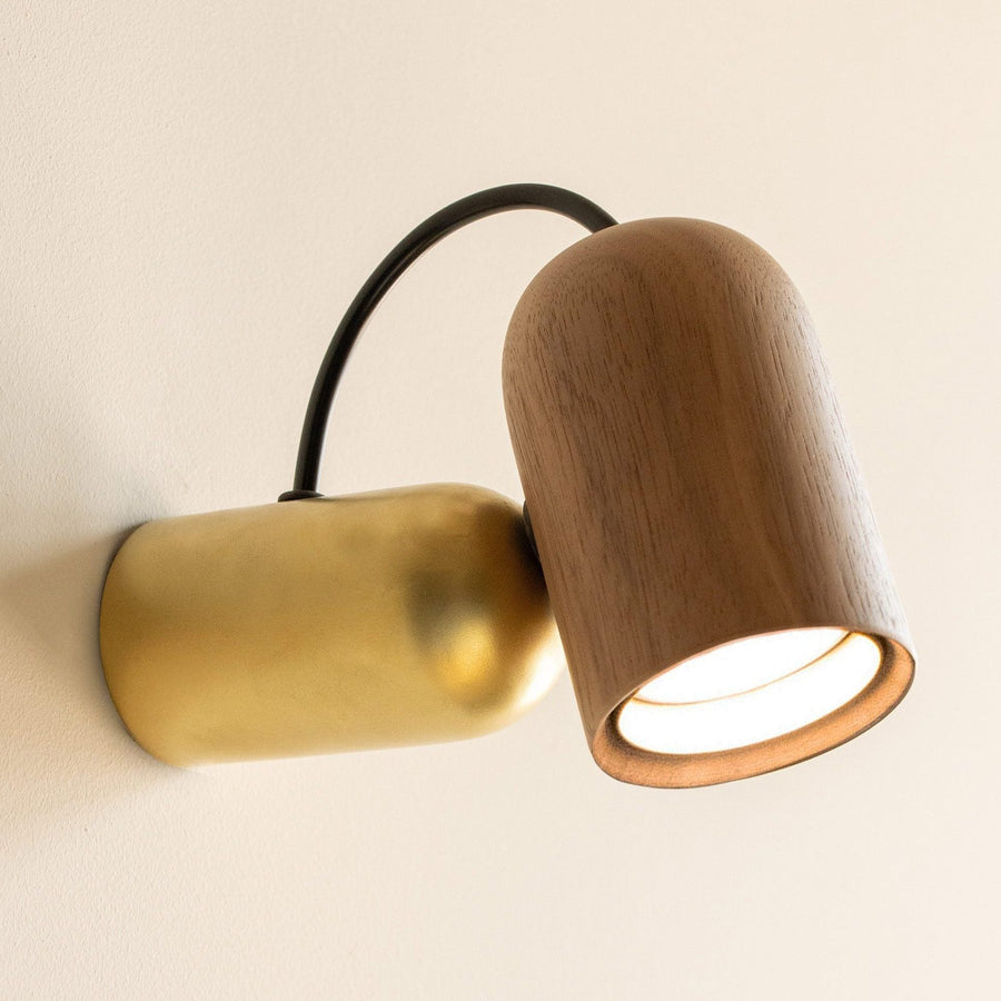 Wall-mounted lamp with wooden and brass finish on a beige background from Nomon available at Spacio retail stores in India. 